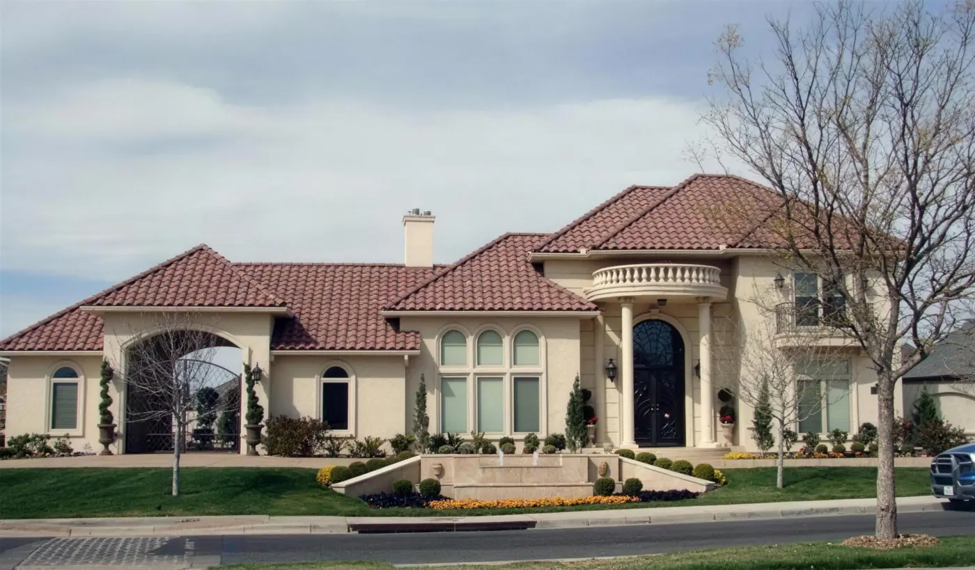 A large stucco house with a red tile roof, a round balcony and a fountain in the front garden.